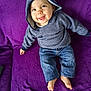 baby, barefoot, casual_wear, cheerful, child, clothing, cozy_clothing, cute, denim_pants, face, happy, hoodie, indoor, infant, person, portrait, purple_blanket, sitting, smiling, young_child