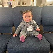 Isabella is registered to the contest to win money with this photo: baby, child, pigtails, smiling, sitting, chair, blue_chair, grey_outfit, totoro_graphic, pink_socks, indoor, carpet, clock, wall_art, person, cute, happy, cozy, room, furniture