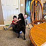 carpet, casual_clothing, child, dog, door, family, floor, glasses, happy, home, hugging, indoor, light_switch, pet, plant, sitting, smiling, socks, table, wooden_chair