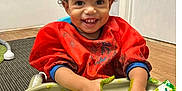 Peyton is registered to the contest to win money with this photo: toddler, child, smiling, painting, finger_paint, red_smock, curly_hair, high_chair, indoor, wooden_floor, carpet, art_activity, messy_hands, happy, creative, playful, person, young_child, expression, colorful