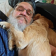 Appy participe au concours pour gagner de l'argent avec cette photo : man, dog, beard, glasses, hug, pet, indoor, chair, leather, casual, comfort, affection, fur, blue_shirt, resting, close_up, adult, expression, home, cuddle
