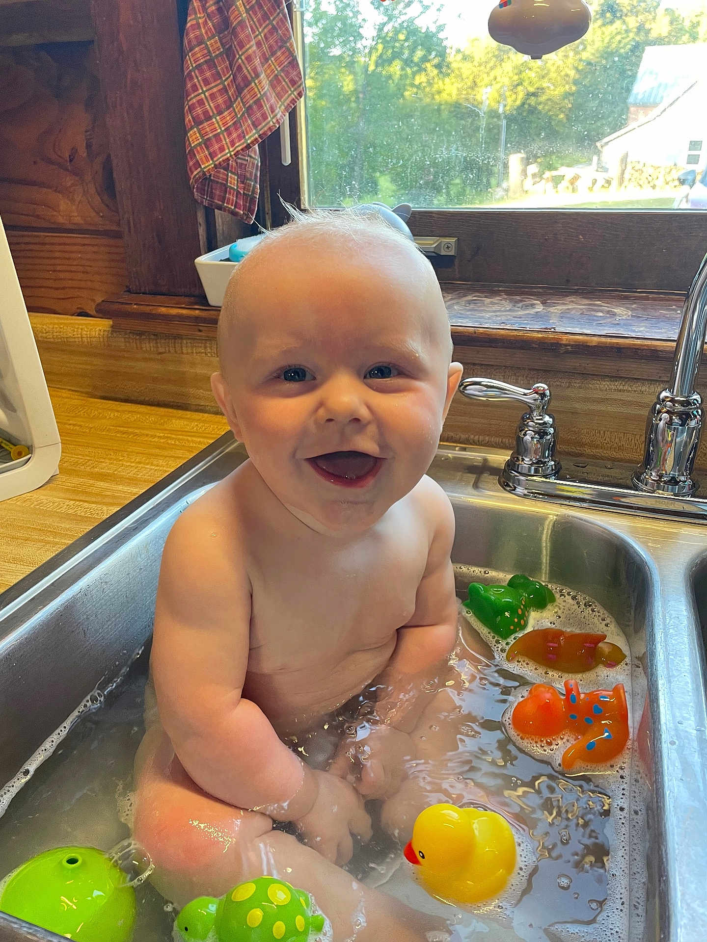 Levi is registered to the contest to win money with this photo: baby, child, sink, water, bath, toys, rubber_duck, kitchen, window, smile, happy, play, toddler, indoor, cute, person, plastic_toys, water_bubbles, daylight, faucet