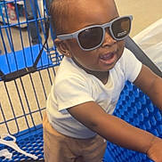 Dasaih is registered to the contest to win money with this photo: baby, child, sunglasses, shopping_cart, store, aisle, person, standing, clothing, pants, white_shirt, blue, floor, earrings, smiling, cute, indoor, retail, shopping, accessory