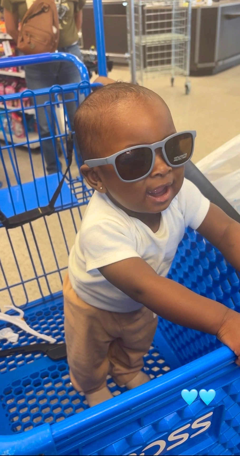 Dasaih is registered to the contest to win money with this photo: baby, child, sunglasses, shopping_cart, store, aisle, person, standing, clothing, pants, white_shirt, blue, floor, earrings, smiling, cute, indoor, retail, shopping, accessory