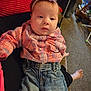 baby, child, plaid_shirt, denim_jeans, headband, purple_bow, person, indoor, carpet, living_room, foot, hand, couch, casual_clothing, seated, infant, expression, young_child, relaxed, soft_lighting