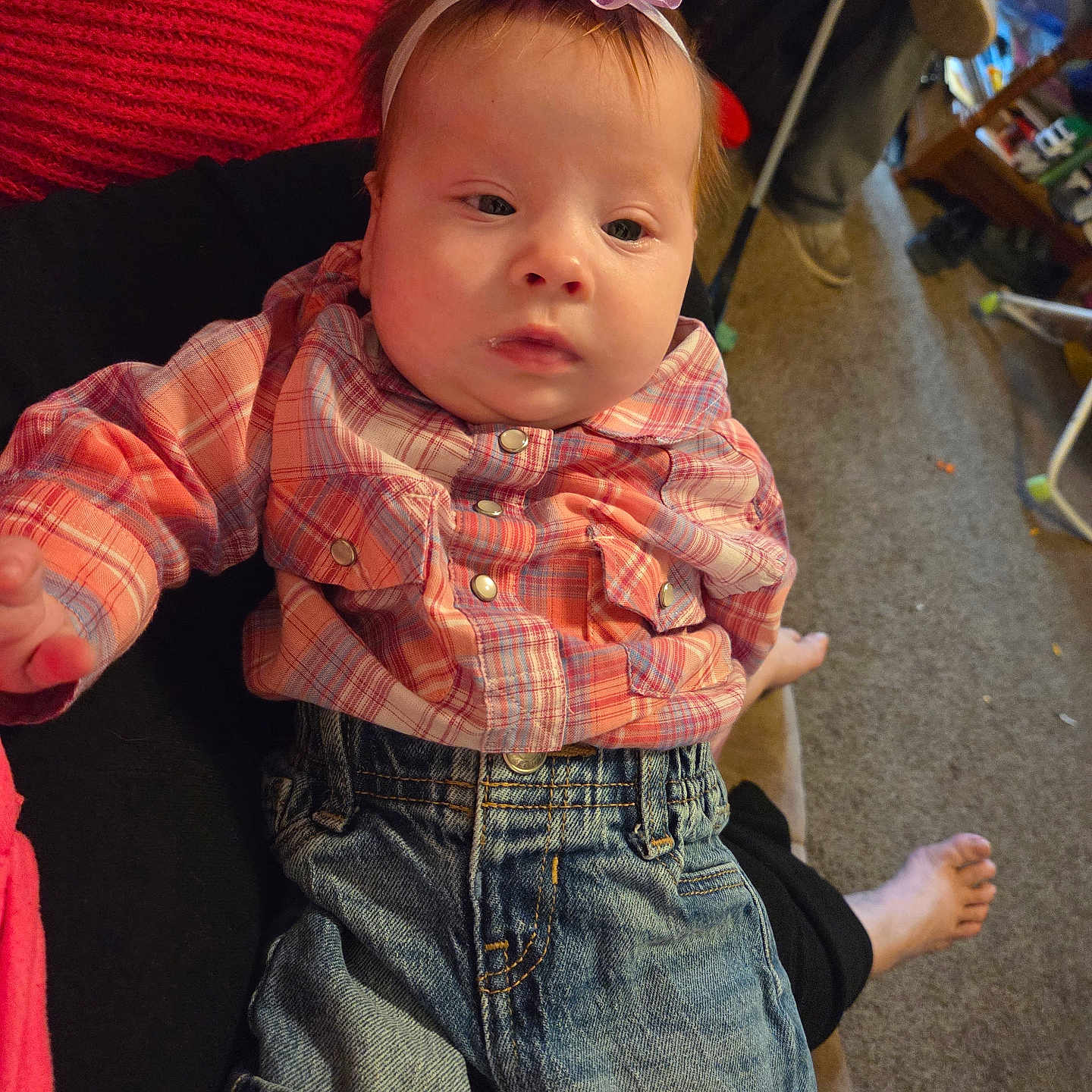 Jade is registered to the contest to win money with this photo: baby, carpet, casual_clothing, child, couch, denim_jeans, expression, foot, hand, headband, indoor, infant, living_room, person, plaid_shirt, purple_bow, relaxed, seated, soft_lighting, young_child