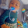 baby, pacifier, toy, blanket, couch, child, infant, clothing, striped_shorts, blue_top, indoor, face, smile, hand, comfort, play, soft_toys, colorful, relaxing, sparkle_effect