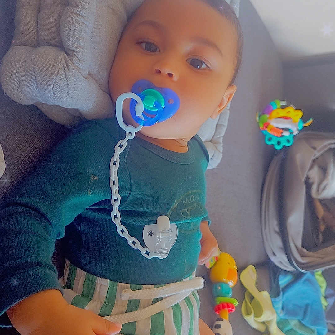 Ngolo participe au concours pour gagner de l'argent avec cette photo : baby, pacifier, toy, blanket, couch, child, infant, clothing, striped_shorts, blue_top, indoor, face, smile, hand, comfort, play, soft_toys, colorful, relaxing, sparkle_effect