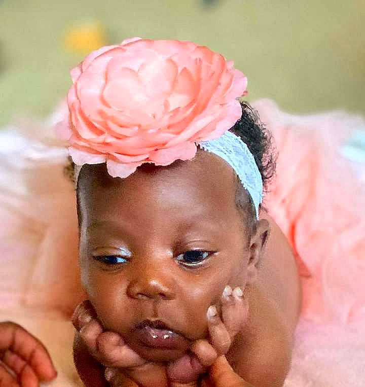 Zoey is registered to the contest to win money with this photo: baby, bathing, child, close_up, eyelash, face, finger, flower, gesture, hair_accessory, happy, head, headband, headpiece, iris, jewellery, person, petal, pink, thumb