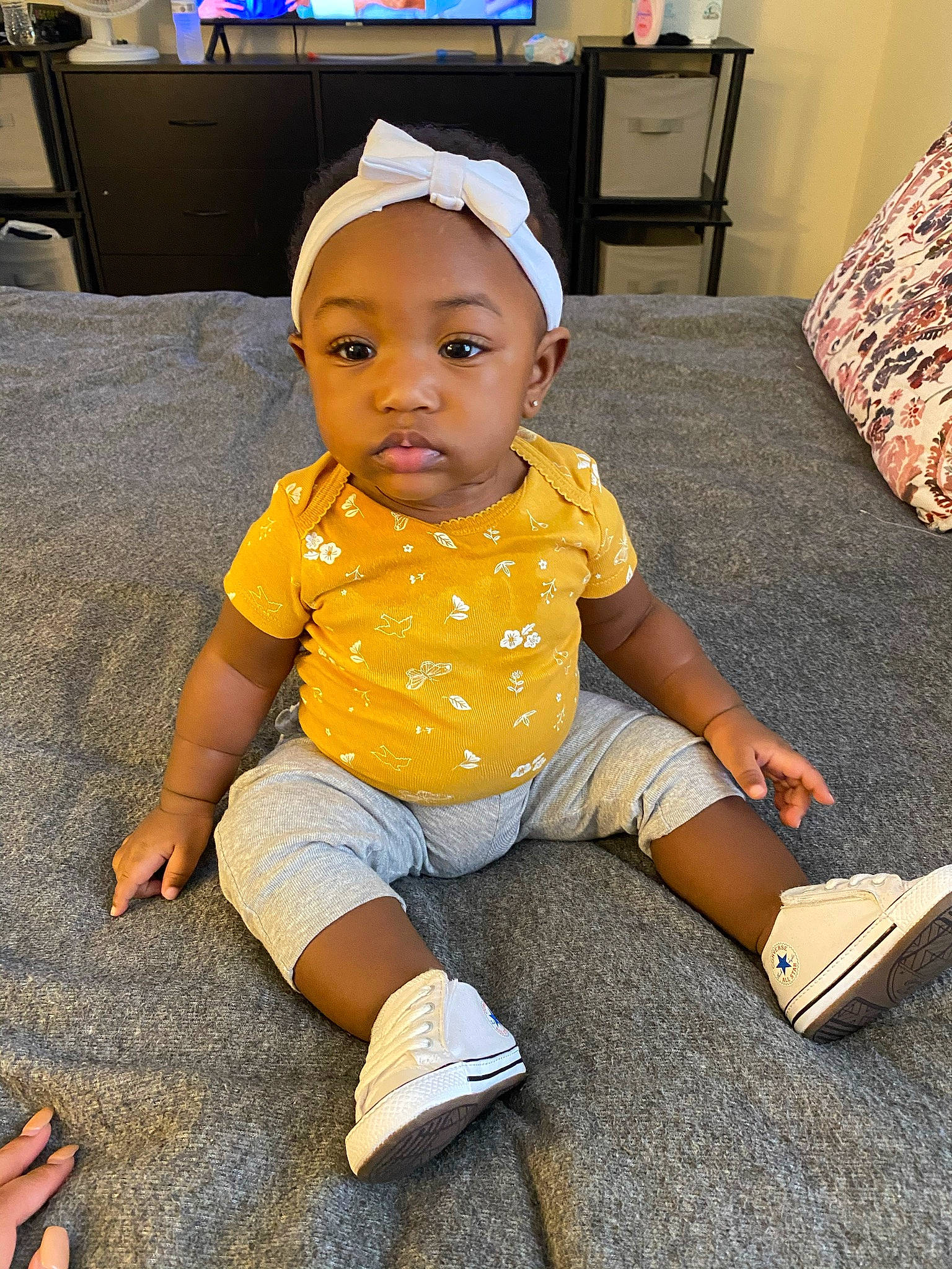 Camille is registered to the contest to win money with this photo: baby, baby_toddler_clothing, cap, chest_of_drawers, child, computer_monitor, couch, desk, floor, flooring, foot, fun, happy, home_appliance, human_leg, person, shorts, sitting, sleeve, sneakers