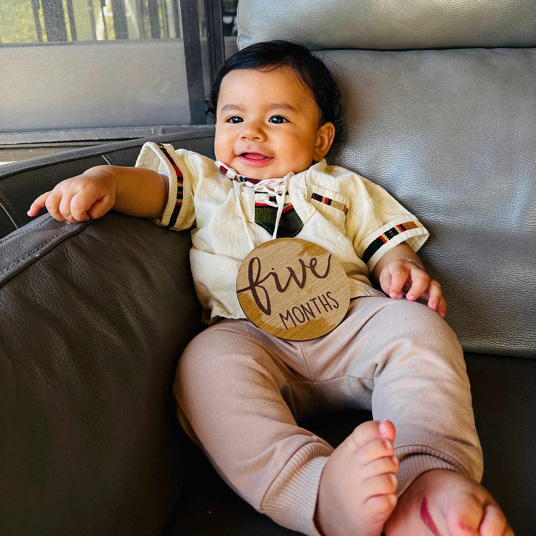 Diego joined the competition — help win amazing prizes! baby, infant, smiling, sitting, couch, leather, indoors, cute, child, clothing, sign, wooden, happy, portrait, feet, hand, face, black_hair, casual, cozy