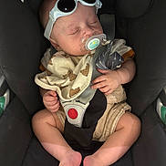Naël participe au concours pour gagner de l'argent avec cette photo : accessory, baby, bib, car_seat, child, clothing, cute, fabric, feet, hands, indoor, infant, pacifier, person, relaxed, safety, seatbelt, sleeping, sunglasses, teddy_bear