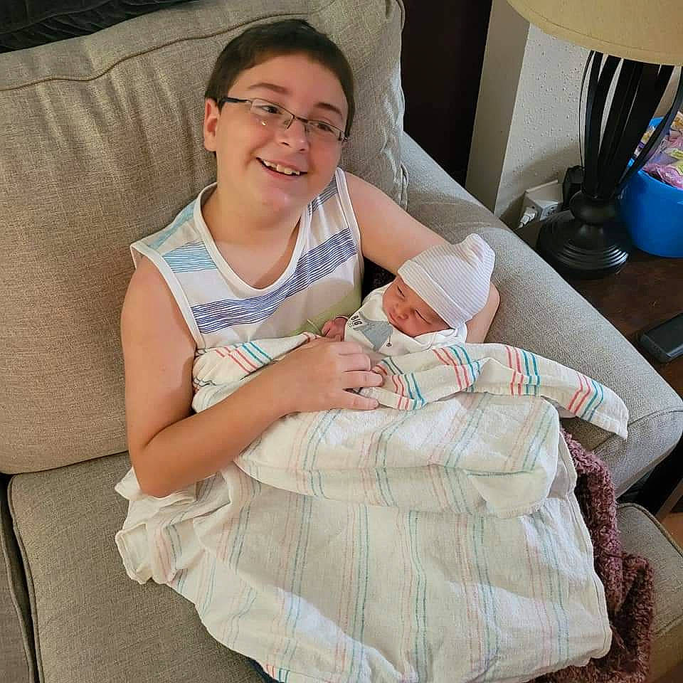 Lexton is registered to the contest to win money with this photo: baby, comfort, couch, event, eyewear, face, glasses, happy, head, headwear, hospital_bed, human_body, human_leg, joy, knee, lap, linens, person, room, smile