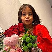 Anais a rejoint le concours — aidez-le/la à gagner de superbes lots ! child, girl, flowers, bouquet, red_shirt, dinosaur_print, puckered_lips, indoor, portrait, dark_hair, green_flowers, pink_roses, red_roses, playful_expression, wall, casual_clothing, person, flower_arrangement, plant, leaf