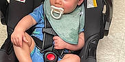 Joni is registered to the contest to win money with this photo: baby, baby_gear, blue_clothing, car_seat, child, child_in_car_seat, child_safety, child_seat, cute, floor, green_bib, indoor, infant, infant_care, pacifier, person, resting, seatbelt, tiled_floor, young_child
