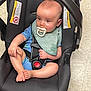 baby, baby_gear, blue_clothing, car_seat, child, child_in_car_seat, child_safety, child_seat, cute, floor, green_bib, indoor, infant, infant_care, pacifier, person, resting, seatbelt, tiled_floor, young_child