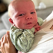 Riley joined the competition — help win amazing prizes! baby, infant, child, person, face, hand, clothing, dinosaur_pattern, green_clothing, holding, close_up, portrait, soft_lighting, indoor, human, cute, newborn, expression, skin, toddler