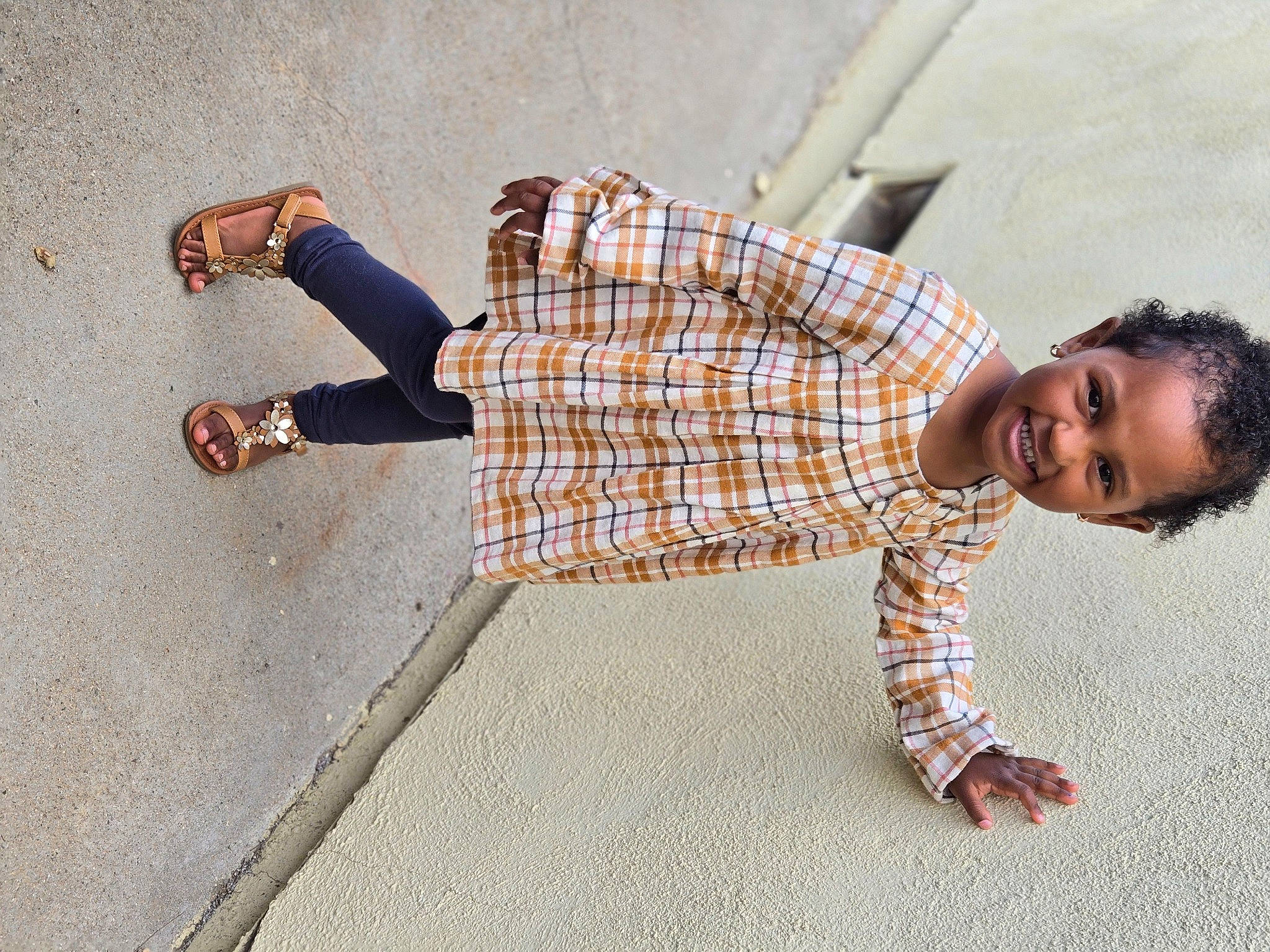 Adrina Love is registered to the contest to win money with this photo: dress_shirt, flooring, foot, fun, happy, human_leg, joy, knee, leg, pattern, person, plaid, road_surface, sidewalk, sitting, smile, street, tartan, thigh, toddler