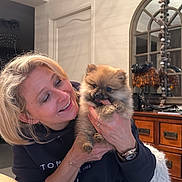 Alden a rejoint le concours — aidez-le/la à gagner de superbes lots ! woman, puppy, dog, indoor, smiling, holding, furniture, mirror, wooden_dresser, table, watch, bracelet, black_clothing, happy, pet, cute, playful, blonde_hair, cozy, nibble