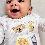 Hunaid is registered to the contest to win money with this photo: baby, smiling, infant, closeup, white_clothing, embroidered_animals, koala, giraffe, lion, zebra, soft_texture, happy, cute, portrait, child, lying_down, indoors, young_child, sleepy_friends, cozy