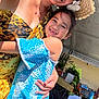 adult, blue_dress, celebration, child, family, floral_pattern, flower_accessory, girl, happy, hat, hug, outdoor, plants, portrait, smile, summer, sunlight, table, tent, woman
