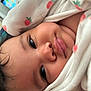 baby, close_up, face, blanket, strawberry_pattern, soft_texture, child, portrait, cute, cozy, indoor, infant, sleepwear, eyelashes, skin, cheeks, nose, mouth, expression, wrapped