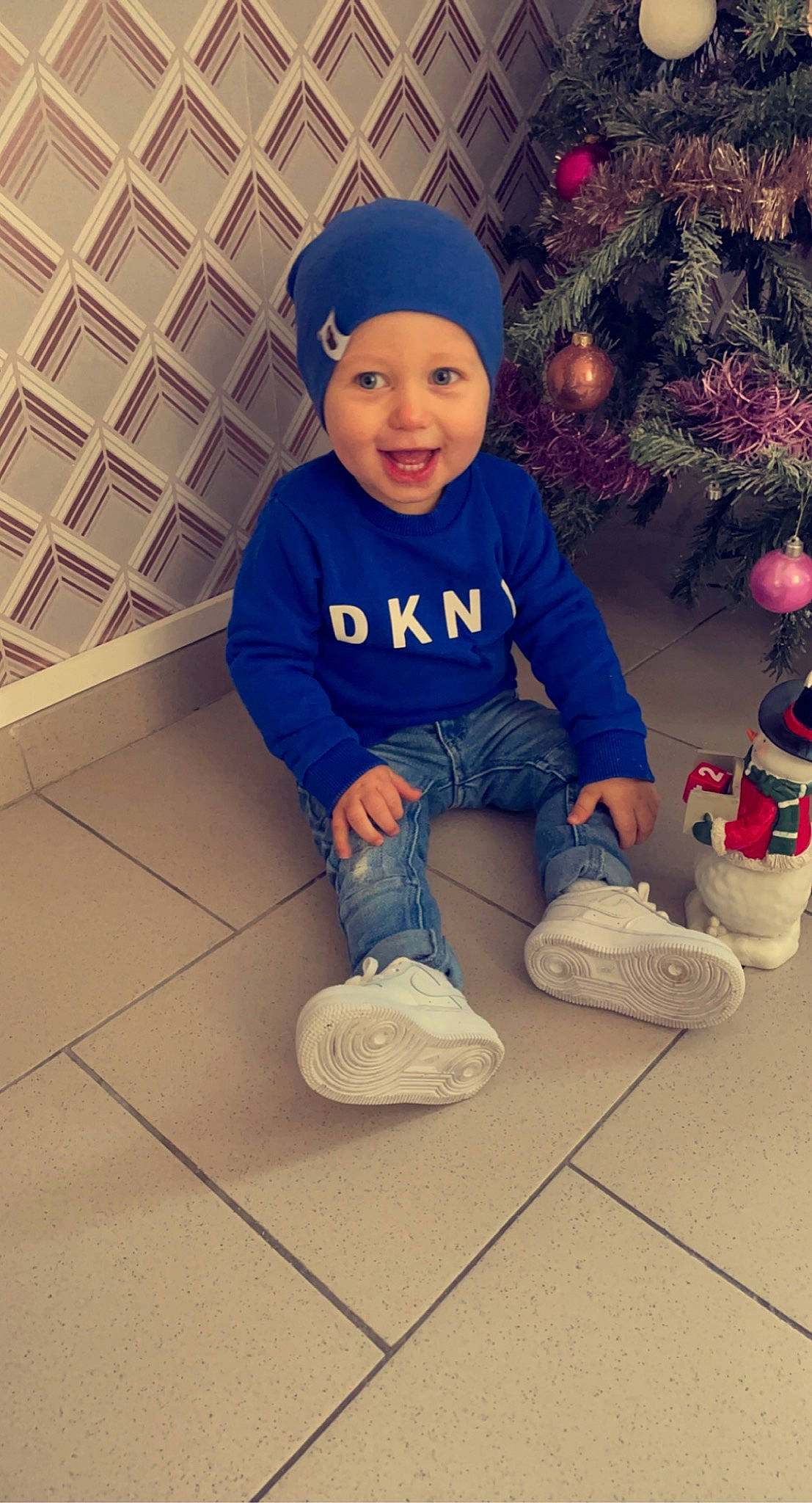 Lenzo participe au concours pour gagner de l'argent avec cette photo : baby, baby_toddler_clothing, baseball_cap, cap, child, christmas_ornament, christmas_tree, electric_blue, face, happy, head, headwear, human_body, light, lighting, person, shoe, sleeve, smile, sock