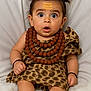 baby, child, surprised, leopard_print, necklaces, beads, pigtails, hair_style, bracelets, sitting, barefoot, cute, portrait, indoors, soft_background, expression, infant, clothing, person, face