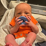 Thomas joined the competition — help win amazing prizes! baby, infant, pacifier, orange_clothing, blanket, diaper, hand, foot, face, newborn, indoor, table, bottle, laptop, technology, person, closeup, sitting, soft_fabric, home