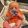 baby, infant, pacifier, orange_clothing, blanket, diaper, hand, foot, face, newborn, indoor, table, bottle, laptop, technology, person, closeup, sitting, soft_fabric, home