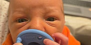 Thomas is registered to the contest to win money with this photo: baby, infant, pacifier, hands, face, orange_clothing, close_up, curious, newborn, skin, cute, portrait, indoor, human, small_fingers, expression, child, person, soft_light, background_blur