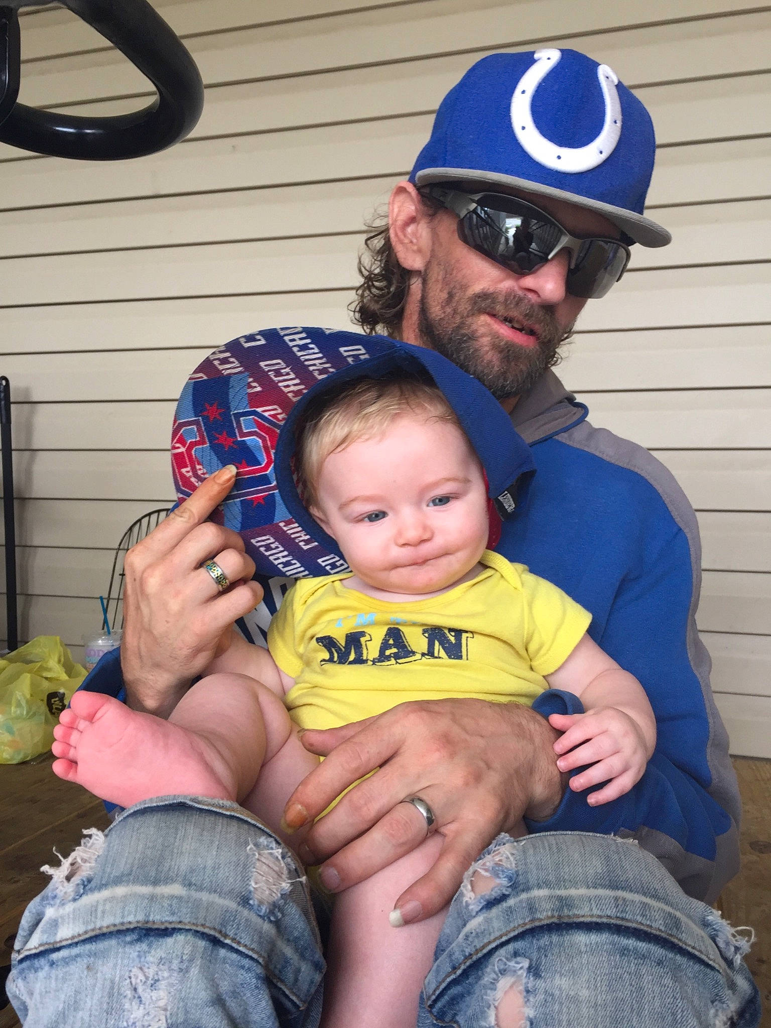 Brett is registered to the contest to win money with this photo: baby, baseball_cap, blue, cap, clothing, eyewear, facial_expression, fun, goggles, green, hairstyle, happy, headwear, jeans, lap, muscle, person, product, sunglasses, thigh