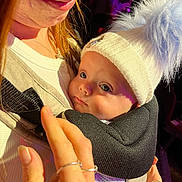 Reggie is registered to the contest to win money with this photo: baby, child, adult, hat, pom_pom, baby_carrier, hand, face, close_up, warm_lighting, skin, clothing, portrait, indoor, gentle, holding, expression, cute, soft_texture, cozy