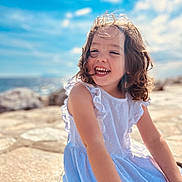 Charlie participe au concours pour gagner de l'argent avec cette photo : child, girl, smiling, curly_hair, white_dress, outdoor, sunny, blue_sky, rocks, happy, portrait, daylight, nature, cute, sitting, joyful, summer, young_child, playful, innocent