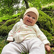 Ellise is registered to the contest to win money with this photo: baby, smiling, forest, moss, greenery, hat, outdoor, nature, child, trees, grass, leaves, happy, cute, infant, clothing, sitting, person, daylight, scenery