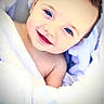 baby, bed, blanket, blue_eyes, brown_hair, child, close_up, cozy, cute, face, happy, indoors, infant, lying_down, photography, portrait, smiling, soft_lighting, swaddled, white_blanket