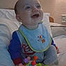 Aryez is registered to the contest to win money with this photo: baby, infant, child, smiling, sitting, bed, bedroom, pillow, blanket, bib, clothing, toy, colorful_toy, rattle, indoor, portrait, happy, face, lamp, cozy