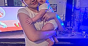 Aryez is registered to the contest to win money with this photo: adult, baby, blue_lighting, butterfly_decor, child, clothing, family, furniture, holding, home, indoor, infant, living_room, mother, parent, portrait, short_sleeves, smiling, television, wall_decor