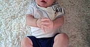 Aryez is registered to the contest to win money with this photo: baby, infant, child, portrait, lying_down, rug, carpet, cream_colored, white_clothing, blue_shorts, hands, feet, wide_eyed, open_mouth, indoors, home, overhead_view, casual_photo, family, safe