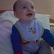 Aryez is registered to the contest to win money with this photo: baby, child, infant, sitting, smiling, face, portrait, indoors, bed, pillows, blanket, bib, clothing, sippy_cup, toy, nursery, home, happy, looking_up, photograph