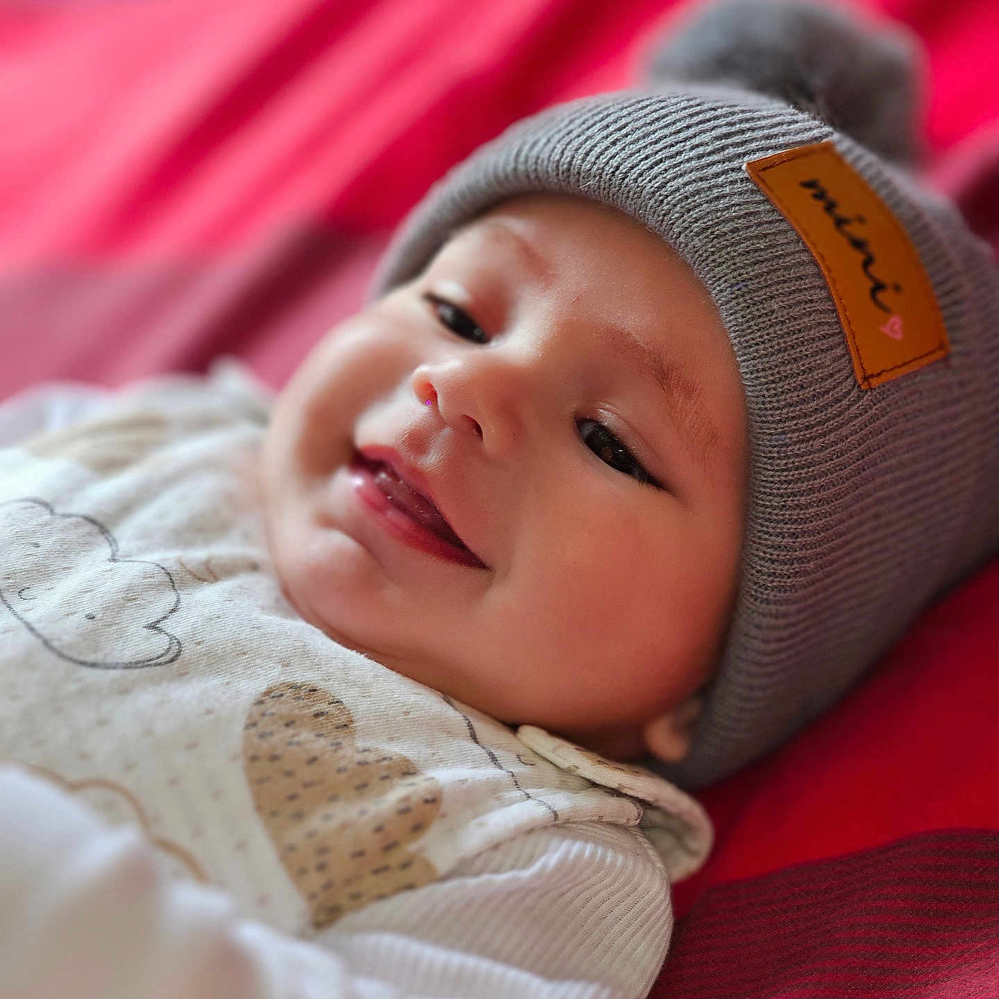 Kenaël participe au concours pour gagner de l'argent avec cette photo : apparel, baby, child, close_up, clothing, cozy, cute, face, happy, hat, indoor, infant, knit_hat, lying_down, pom_pom, portrait, red_blanket, smiling, soft_focus, warm