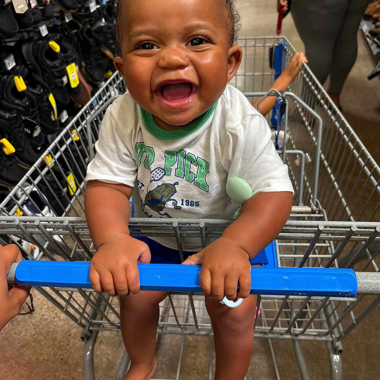 Khaleel is registered to the contest to win money with this photo: adult, baby, blue_handle, child, clothing, face, grocery_cart, happy, indoor, infant, laughing, portrait, retail, seated, shoes, shopping, shopping_cart, smiling, store, t_shirt
