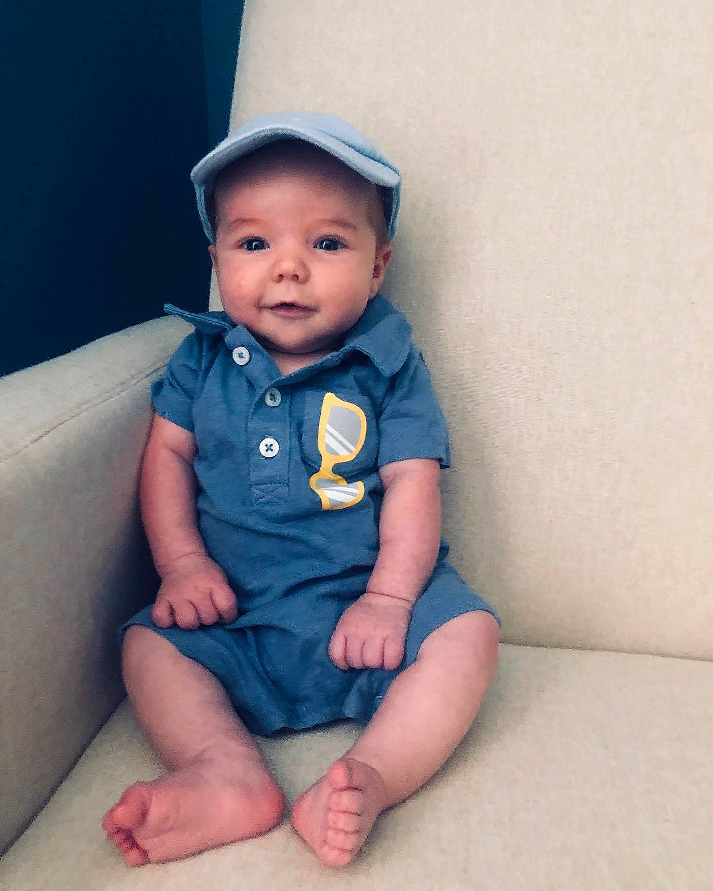 Sutton is registered to the contest to win money with this photo: baby, baby_toddler_clothing, blue, cheek, child, eye, finger, head, headwear, leg, person, sitting, skin, sleeve, smile, standing, toddler