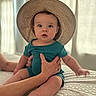 Mac is registered to the contest to win money with this photo: baby, child, infant, hat, straw_hat, teal_clothing, hands, bed, blanket, indoor, person, cute, sitting, portrait, looking_at_camera, skin, face, expression, soft_light, cozy