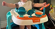 Mac is registered to the contest to win money with this photo: baby, walker, smiling, happy, indoor, toy, child, feet, bib, furniture, floor, person, play, arms_outstretched, head, clothing, home, table, legs, cute