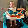 baby, walker, smiling, happy, indoor, toy, child, feet, bib, furniture, floor, person, play, arms_outstretched, head, clothing, home, table, legs, cute