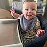 Mac is registered to the contest to win money with this photo: baby, child, smiling, high_chair, bib, happy, indoor, person, face, cheerful, cute, infant, clothing, table, hand, seat, expression, portrait, young, furniture