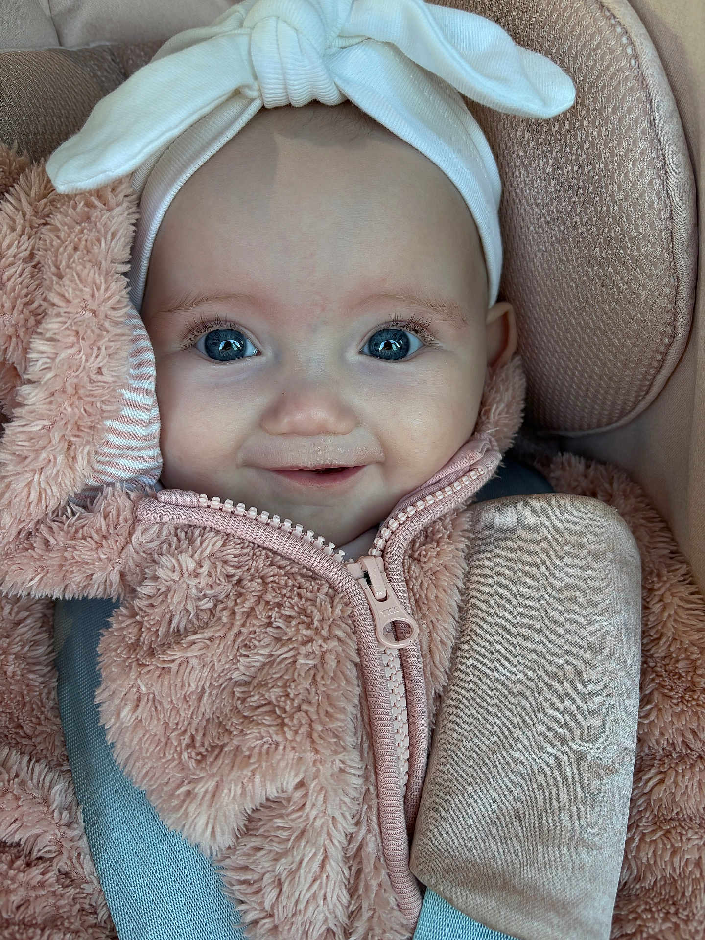 Christine-Rose joined the competition — help win amazing prizes! baby, blue_eyes, bow, car_seat, child, closeup, clothing, cute, face, furry, happy, headband, indoor, infant, jacket, person, pink, portrait, seatbelt, smile