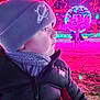 child, hat, jacket, scarf, winter_clothing, outdoor, night, holiday_lights, tree, illumination, decoration, colorful, festive, person, profile, cold_weather, park, grass, puffer_jacket, curious