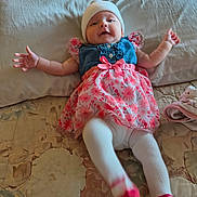 Blair is registered to the contest to win money with this photo: baby, infant, child, bed, blanket, dress, denim, floral_pattern, white_beanie, tights, socks, pink, arms_outstretched, kicking_legs, happy, cute, indoors, portrait, smiling, person